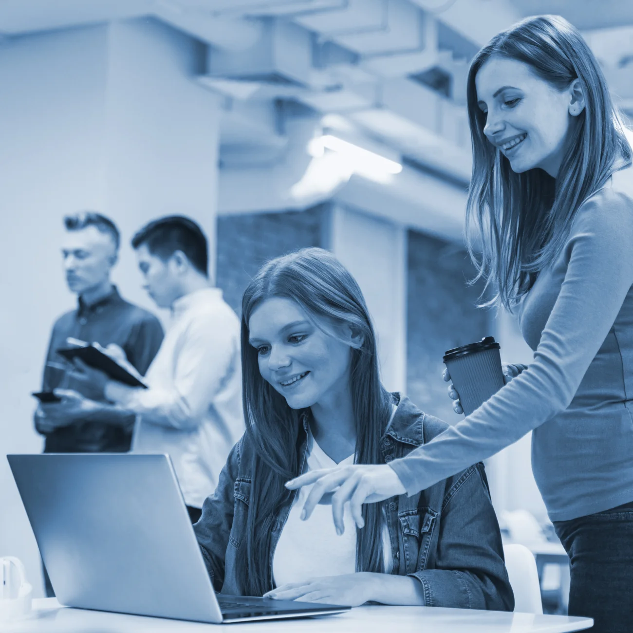 Dos mujeres jóvenes sonriendo mientras revisan laptop en oficina durante proyecto