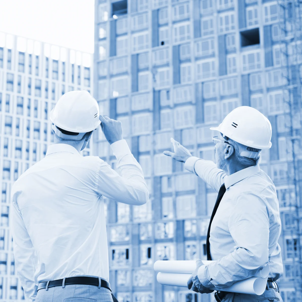 Dos supervisores de construcción con casco de seguridad revisando avance de obra frente a edificio en construcción